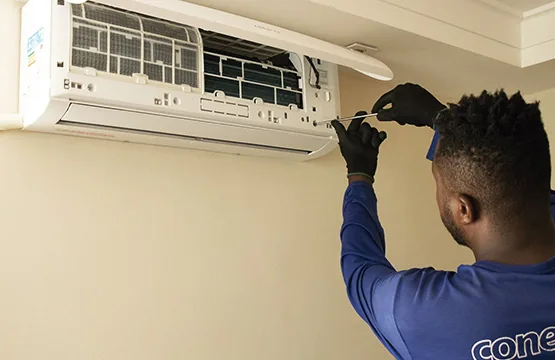 Técnico da Conect Ar, com luvas, ajustando a evaporadora de um ar-condicionado split fixado na parede