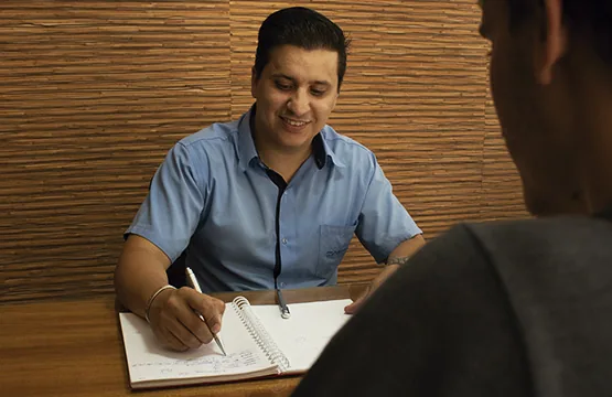 Profissional da Conect Ar atendendo um cliente à mesa, fazendo anotações em caderno durante o levantamento do projeto